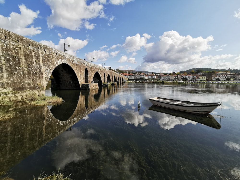 white wooden row boat on clear water near bridge under blue sky and white clouds during day time