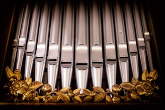 A series of metallic organ pipes arranged in a vertical alignment, featuring intricate golden floral decorations at the base.