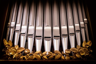 A series of metallic organ pipes arranged in a vertical alignment, featuring intricate golden floral decorations at the base.