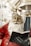 A festive Santa Claus statue holding a book is adorned in a classic red and white outfit, with shiny bells hanging above. The intricate details on Santa’s face and beard, along with the gloved hand holding the book, are well-defined.
