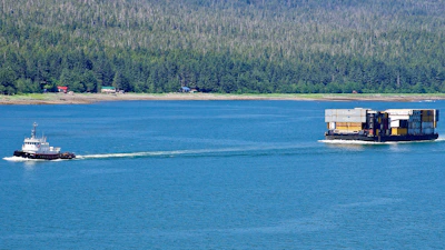 A tugboat guiding a massive container ship through calm waters.