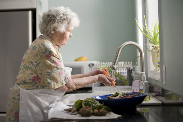 A senior woman washing fresh carrots in her own kitchen
