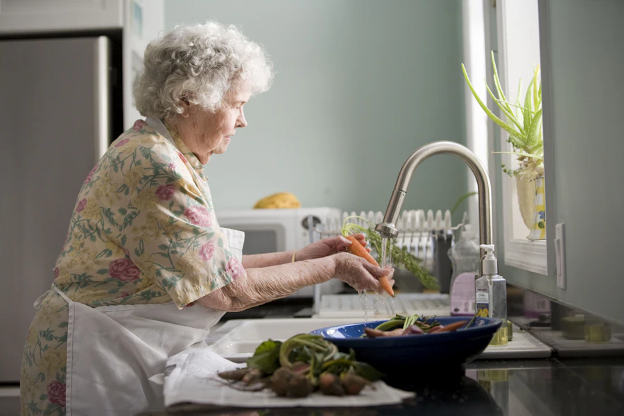 A senior woman washing fresh carrots in her own kitchen at home in Eudora