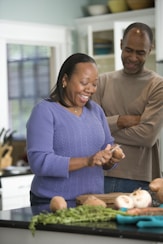 A group of community members smiling while preparing fresh vegetables together in a bright kitchen.