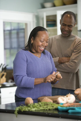 A happy person holding fresh fruits and vegetables, smiling in a bright kitchen.