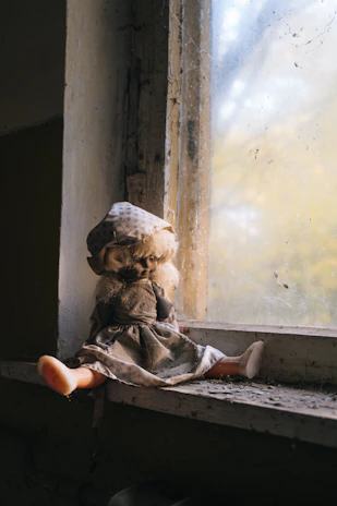 A tasteful scene showing a veloura doll seated by a window with natural light casting gentle shadows.