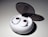 A pair of wireless earbuds resting in an open charging case. The case is white, oval-shaped with a smooth, glossy finish, and a transparent lid. The earbuds have circular touch controls highlighted with a red rim.