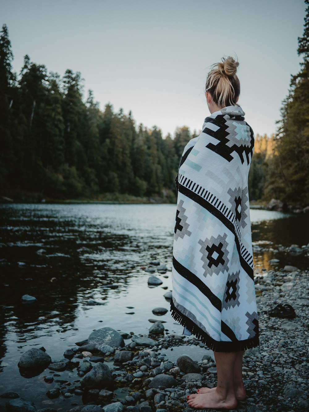 barefooted woman standing while using poncho near river
