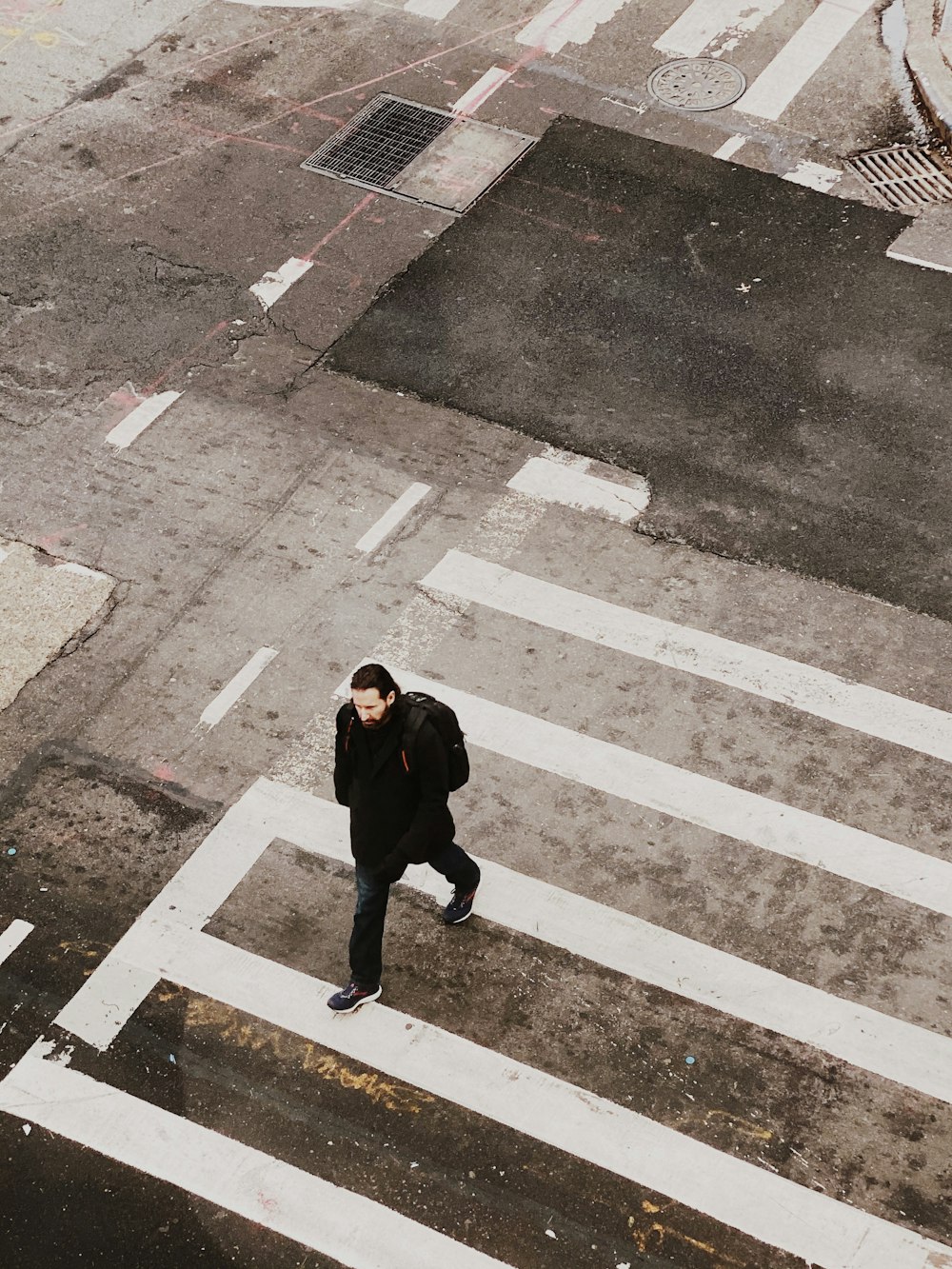man wearing black jacket walking on pedestrian lane
