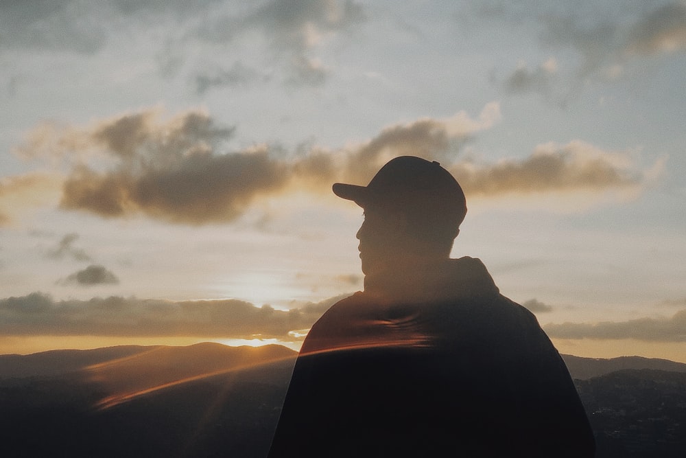 silhouette of man wearing cap looking at mountain sunset