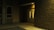 A dimly lit exterior corner of a building featuring a closed double door with narrow windows. The area is surrounded by brick walls, and the ground appears to be paved. A sign indicating handicapped parking is visible to the left near a window.