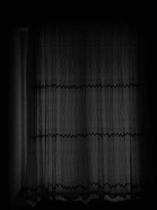 A dark, lace curtain hangs in front of a window, filtering limited light. The curtain features intricate patterns with wavy lines and dots, adding a sense of texture and depth.