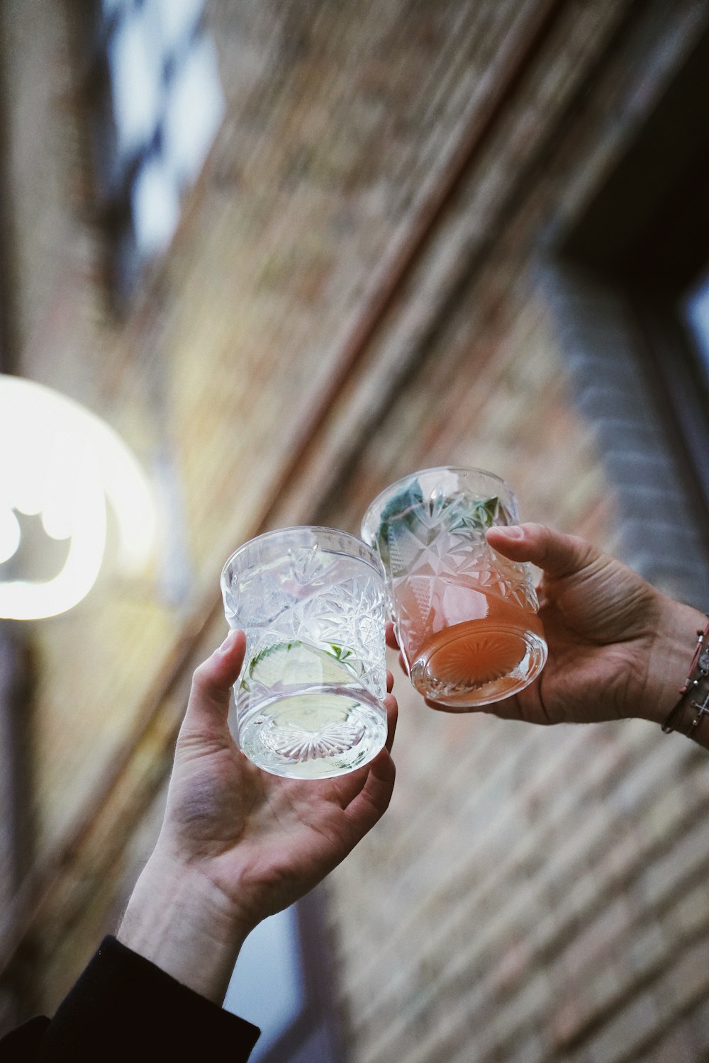 selective focus photo of two hands holding clear drinking glasses