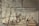 A group of people are engaged in the process of sugar production inside a large industrial building. There is steam rising from the vats, and workers are attending to various tasks such as stirring large pots and inspecting the production process. The atmosphere seems busy and structured, with a focus on labor.