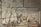 A group of people are engaged in the process of sugar production inside a large industrial building. There is steam rising from the vats, and workers are attending to various tasks such as stirring large pots and inspecting the production process. The atmosphere seems busy and structured, with a focus on labor.