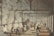 A group of people are engaged in the process of sugar production inside a large industrial building. There is steam rising from the vats, and workers are attending to various tasks such as stirring large pots and inspecting the production process. The atmosphere seems busy and structured, with a focus on labor.