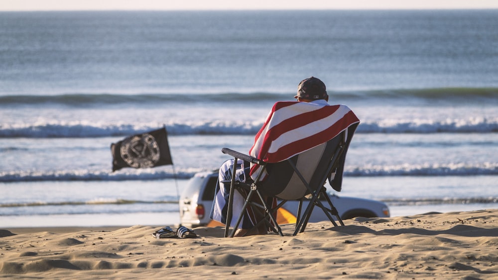 photography of person sits on chair beside seashore during daytime