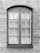 A symmetrical, rectangular window framed with dark wood is set into a textured stone wall. The window consists of two panels, each containing multiple small glass panes separated by white muntins. The surface of the wall appears uneven with visible brush strokes or trowel marks.