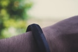A close-up of a person's wrist wearing a black, textured fitness band. The background is blurred with greenish hues, suggesting an outdoor setting.