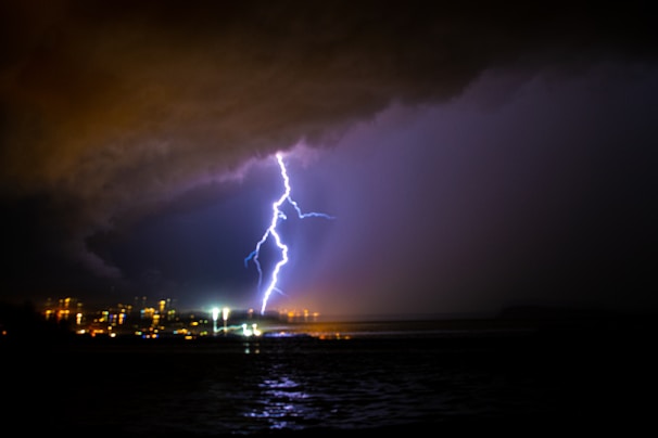 A dramatic lightning bolt striking a dark stormy sky over a cityscape at night.