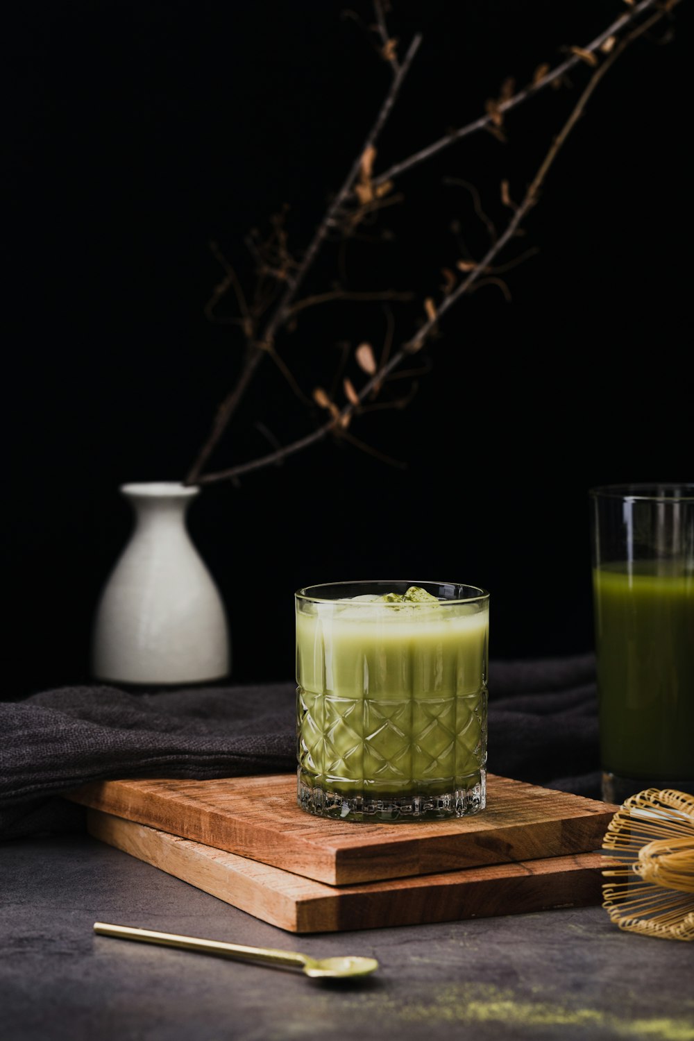 ein Glas grüner Saft neben einem hölzernen Schneidebrett