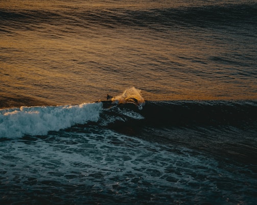 A surfer riding a powerful wave at sunset, with vibrant colors reflecting on the water.
