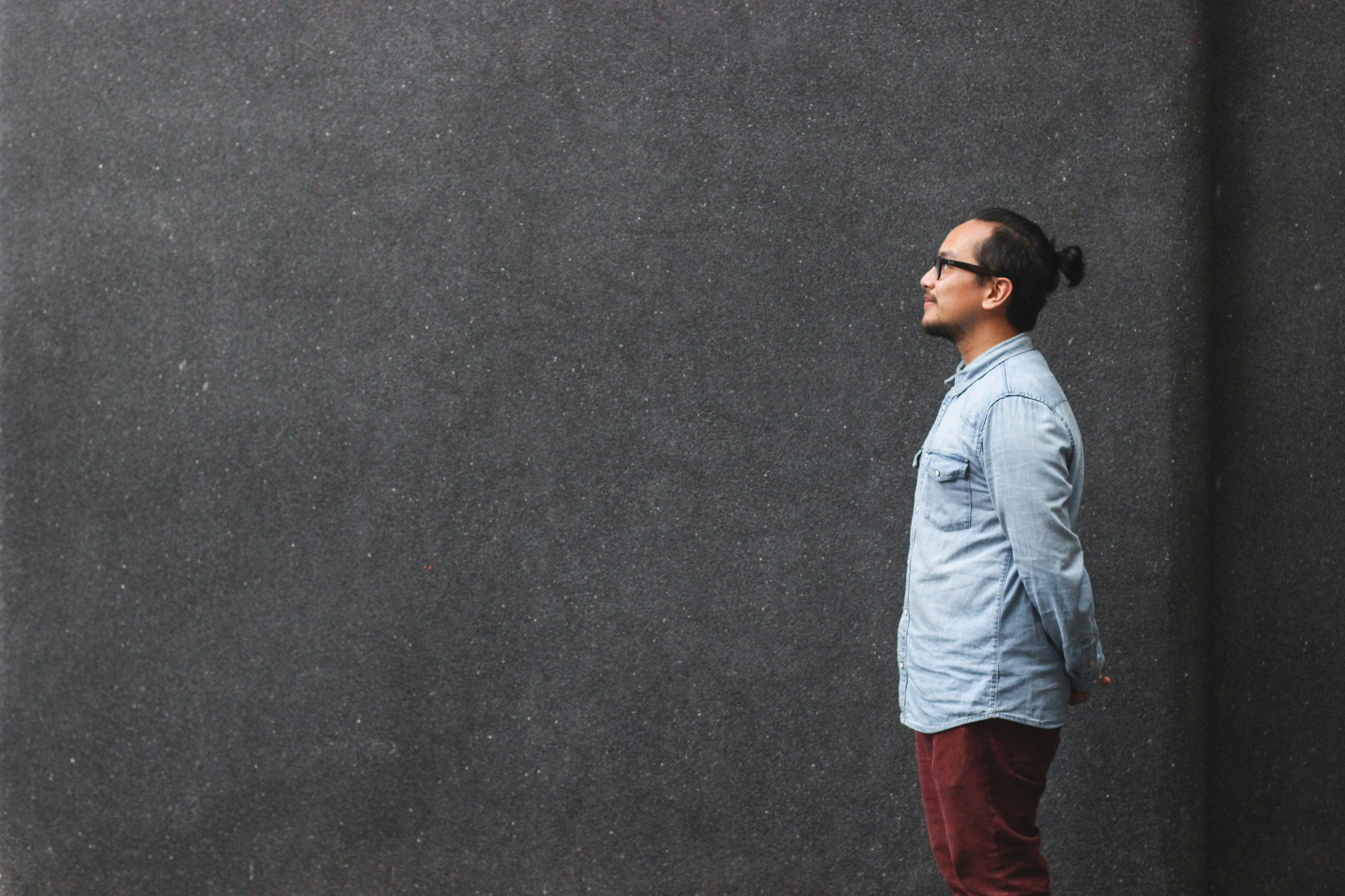 man in blue dress shirt standing beside wall