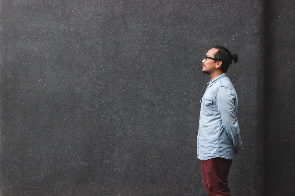 man in blue dress shirt standing beside wall