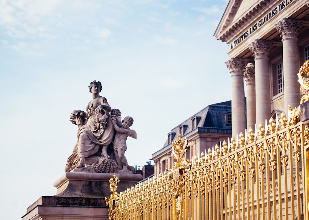 gray woman and cherubs statue in front of building with gold-colored grill fence