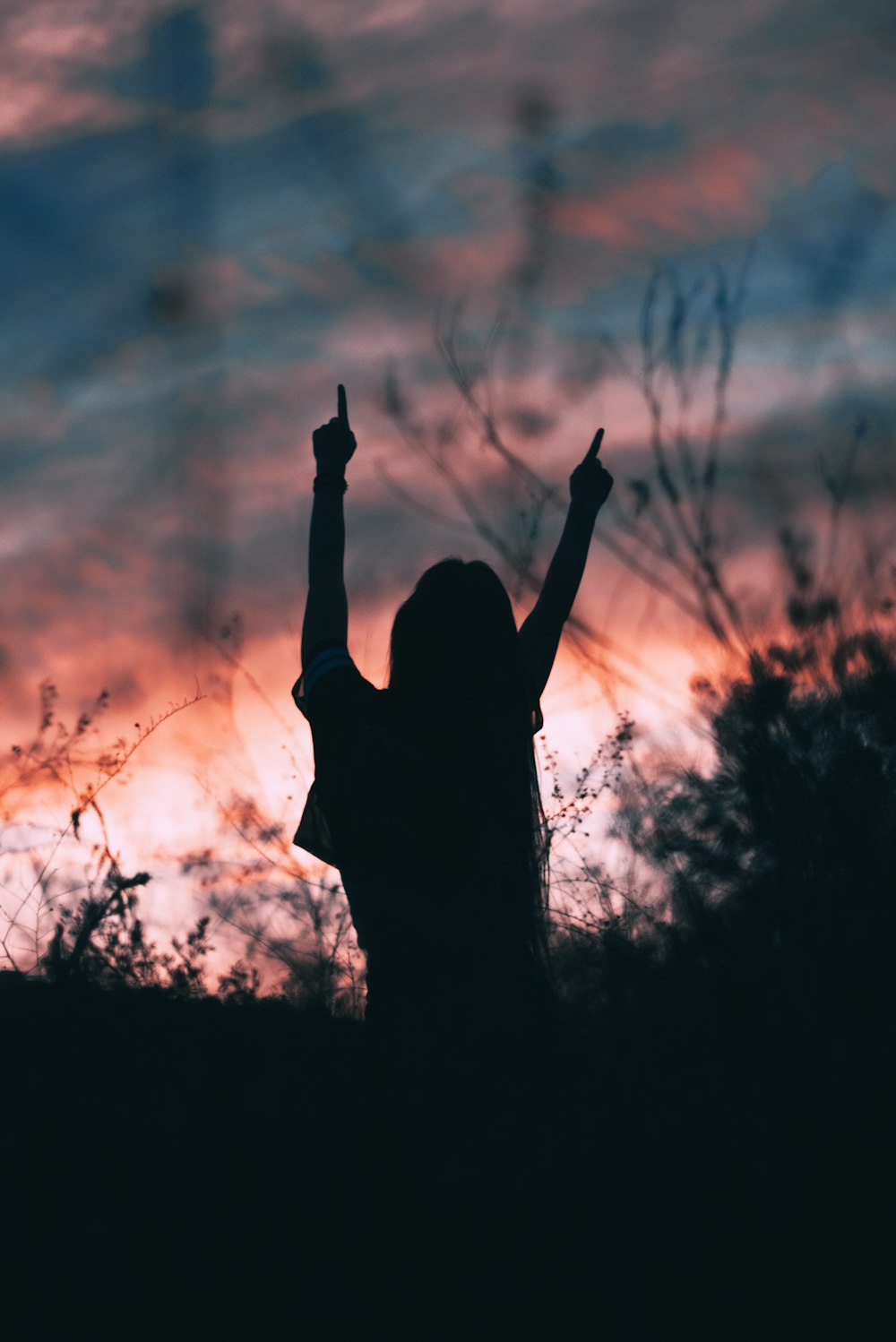 silhouette of woman raising hands facing sun during golden hour