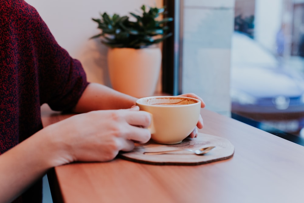 shallow focus photo of person holding brown ceramic mug on table