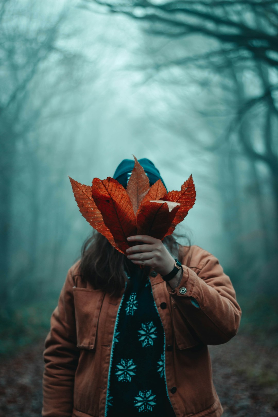 woman wearing orange jacket holding brown leaves