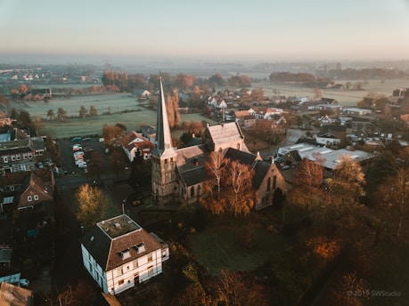 A serene aerial shot of a quiet Iowa town at dawn, with soft golden light spilling over rooftops and fields.