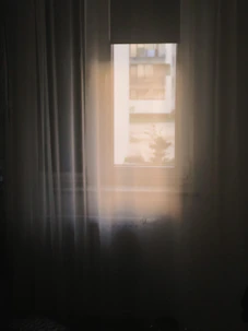 a window in a dark room with a white curtain