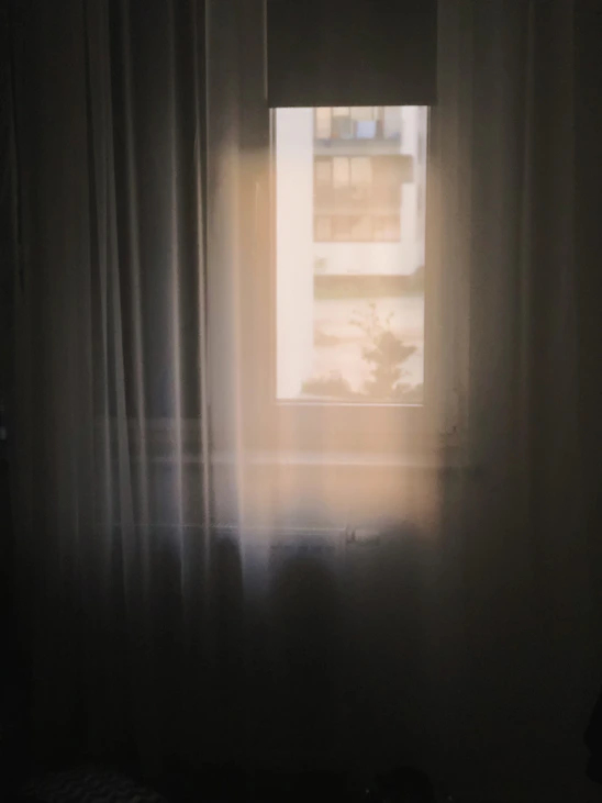 a window in a dark room with a white curtain