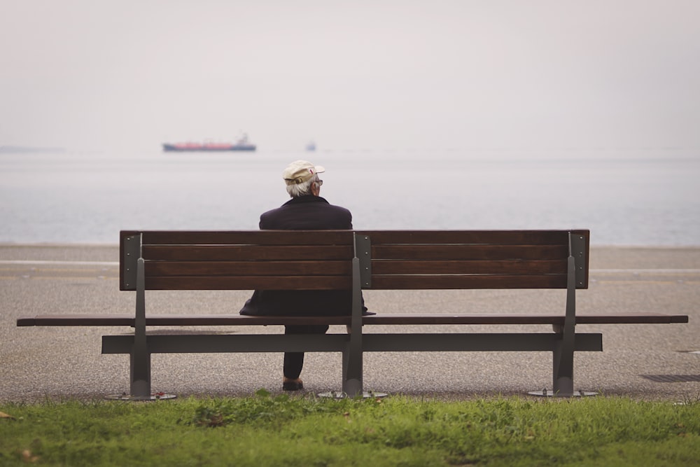 海に面した茶色のベンチに座る男