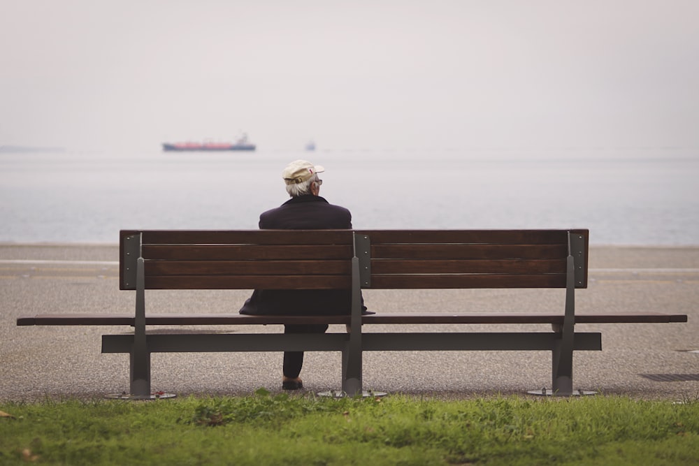 Mann sitzt auf brauner Bank mit Blick auf das Meer