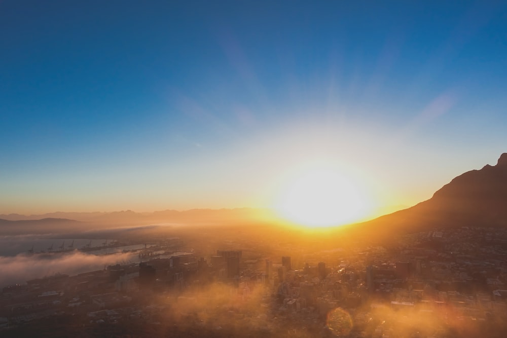 the sun is setting over a city with a mountain in the background