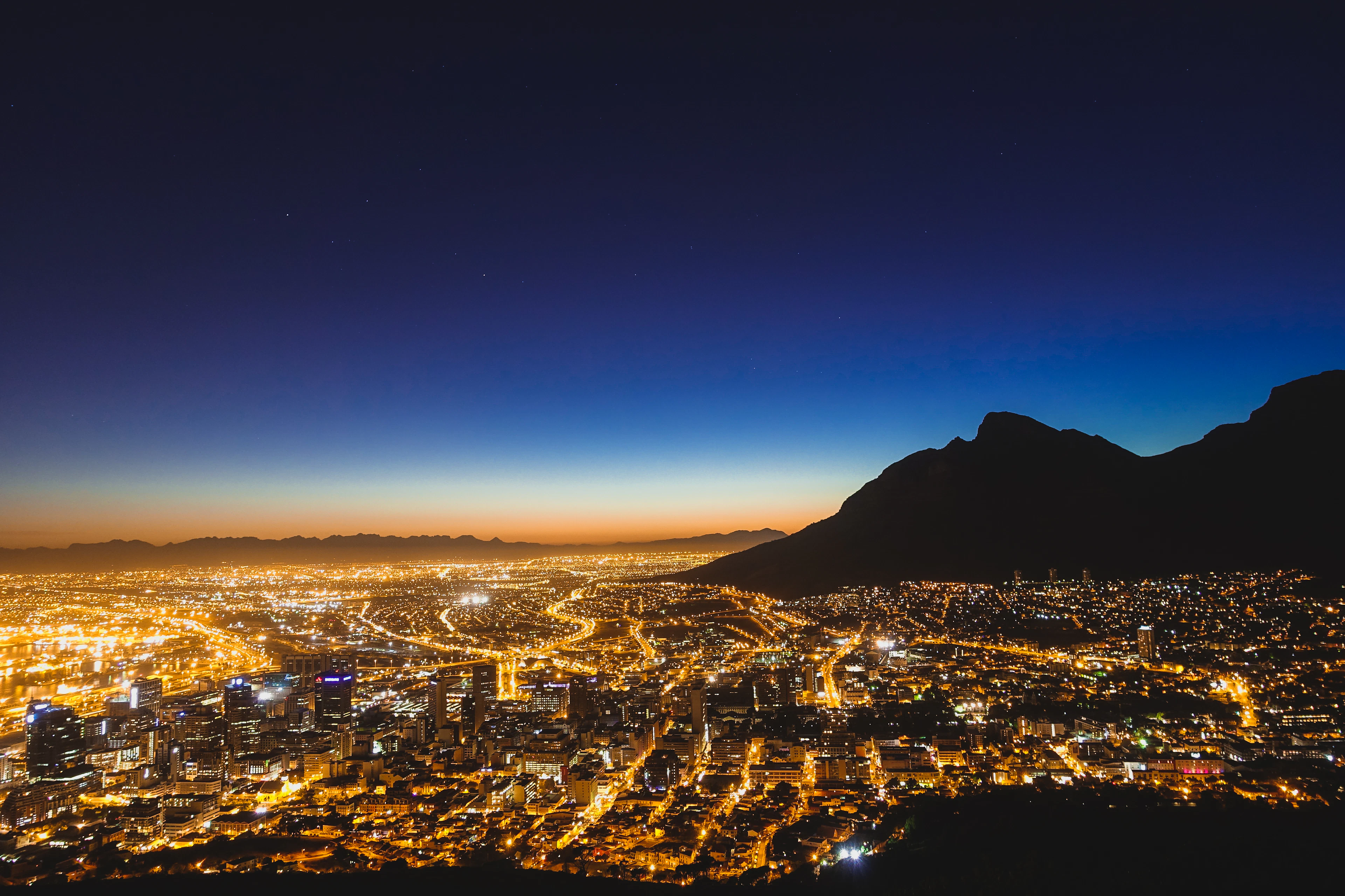 Cape Town's city lights spread beneath a star-lit sky with Table Mountain's dark silhouette alongside.
