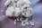 A pile of heart-shaped cookies dusted with powdered sugar, adorned with small heart decorations. Some cookies have chocolate chips embedded in them, and there are loose sugar hearts scattered around.