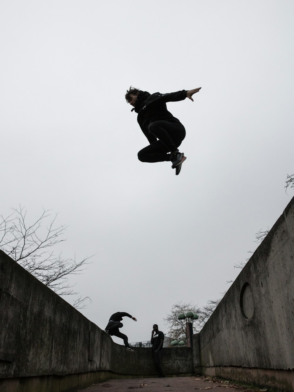 昼間、空中で飛び跳ねる黒いジャケットとズボンの男