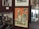 A collection of framed photographs and a colorful vintage poster are displayed on a wall. The poster features illustrations and black and white photos of two people, along with orange and cream stripes.
