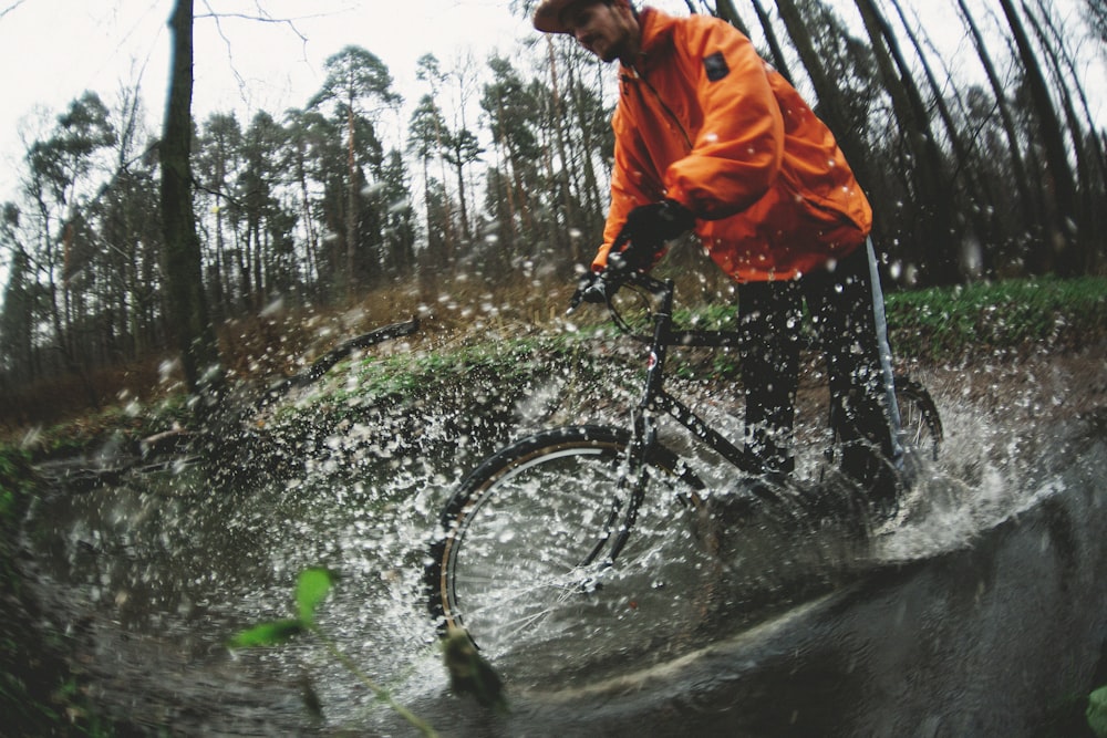man wearing orange zip-up jacket biking on wet road