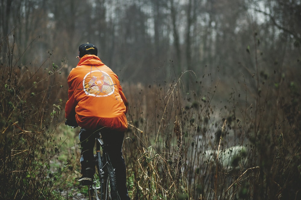 man wearing orange jacket and black pants riding mountain bike