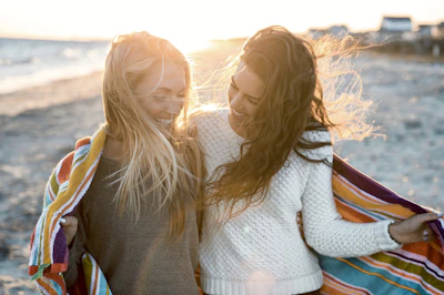 Smiling women wrapped in pink shawls sharing a moment of laughter during a self-love retreat outdoors.