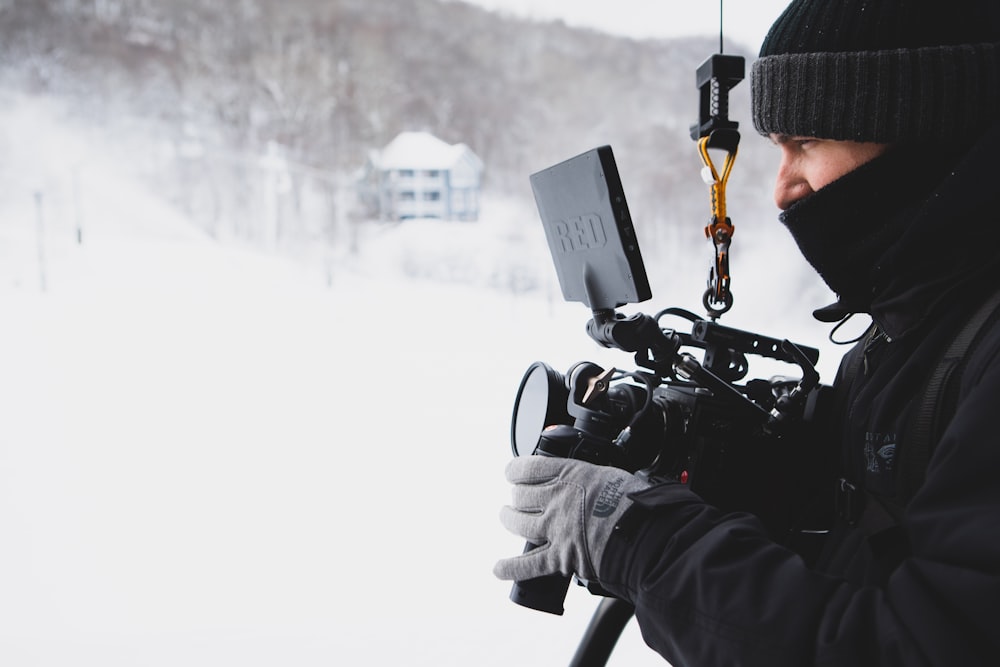 person wearing black jacket and bennies holding video camera