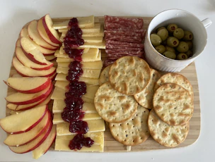 A rustic wooden board displaying an adult lunchable with salami, cheese, and crackers.