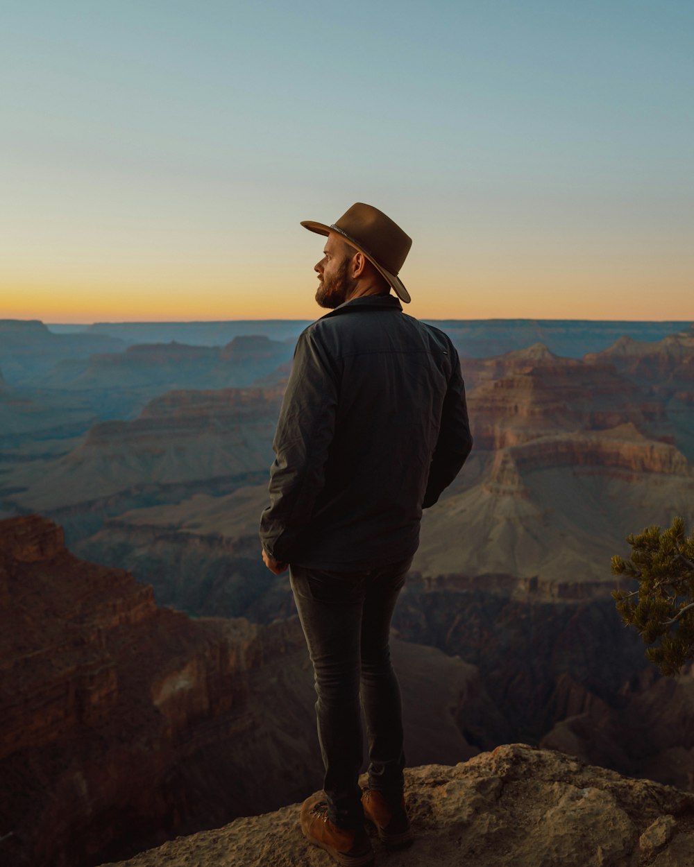 man wearing gray jacket and gray pants standing on mountain edge