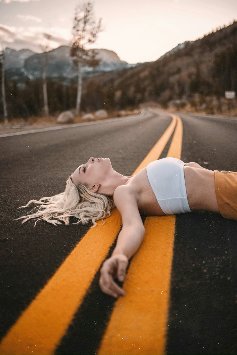 Mujer con crop top blanco acostado en camino asfaltado