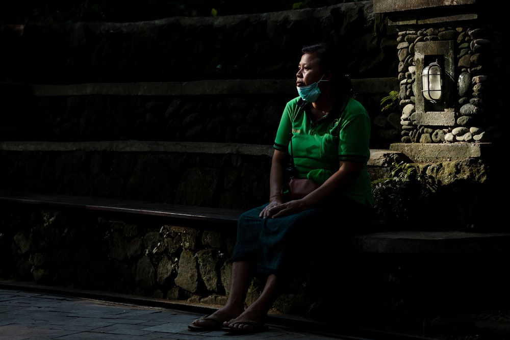 コンクリートのベンチに座る緑色のポロシャツを着た女性